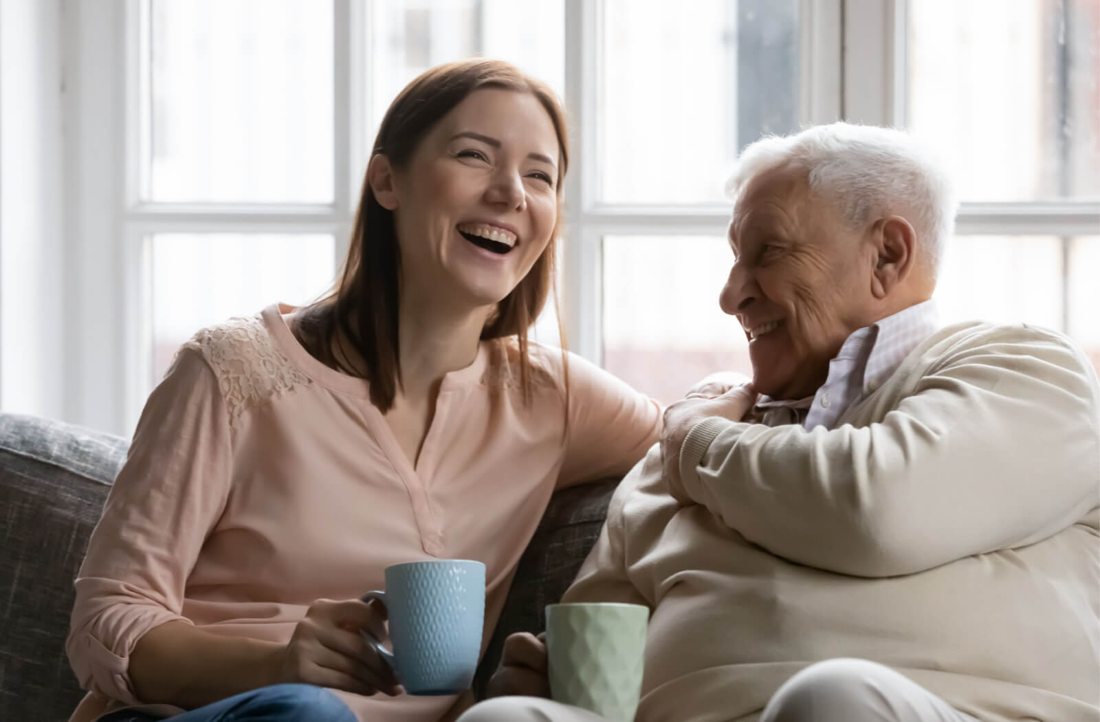 A senior man and his daughter smiling and talking to each other while sitting on a couch.
