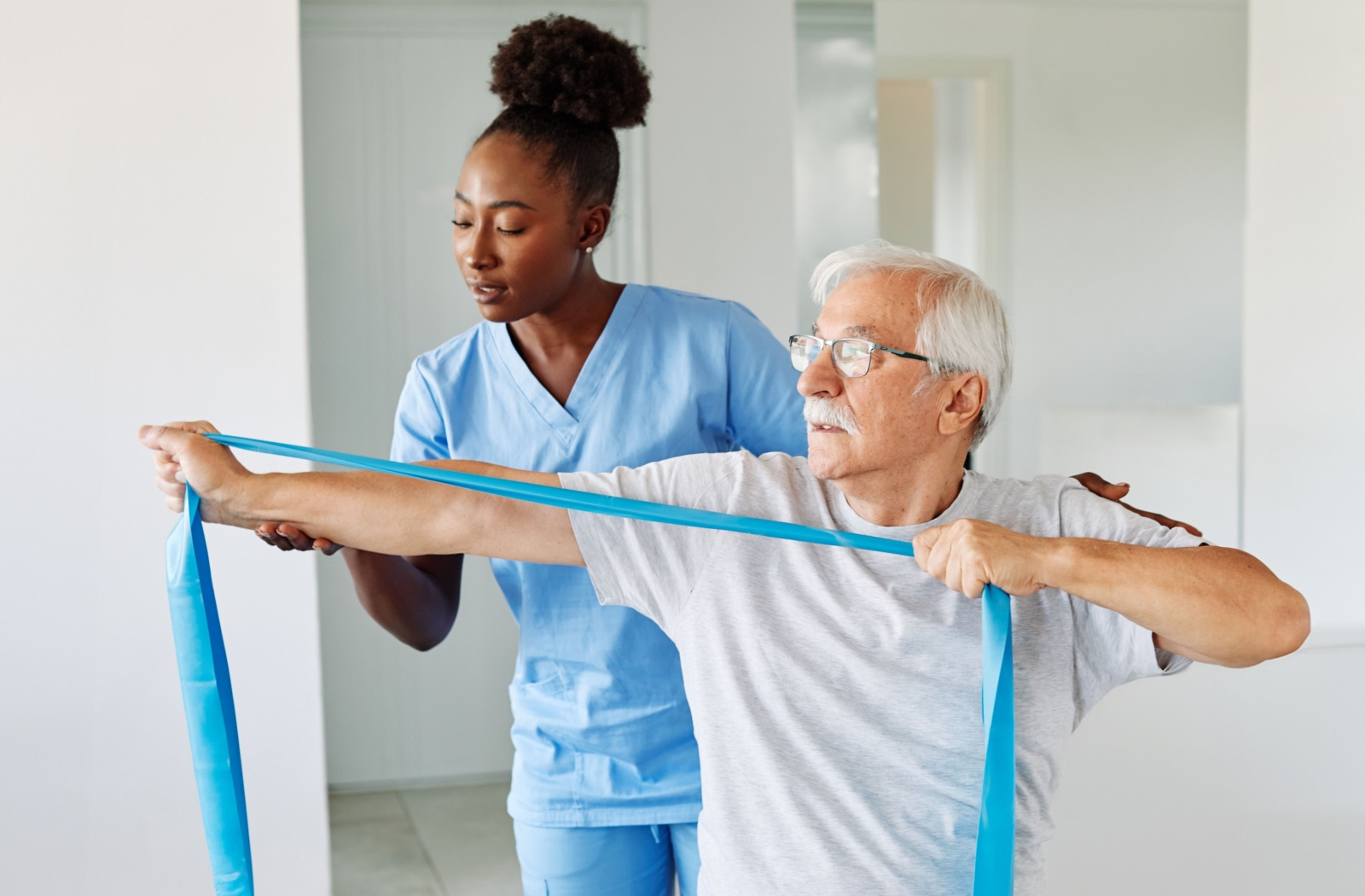 A physical therapist shows an older adult how to strength their upper body to improve posture using a resistance band.