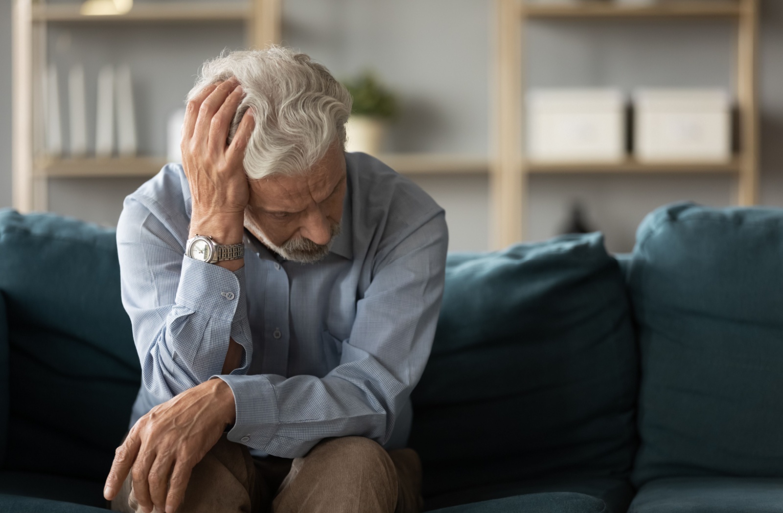 An older adult sitting on the couch and rubbing their forehead in frustration due to stress.