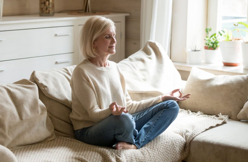 An older adult meditating on their couch in a sunlit living room to lower their stress levels.
