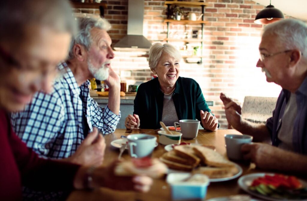 A group of seniors laugh and talk over a shared meal in senior living, provided and designed by nutritionists and chefs