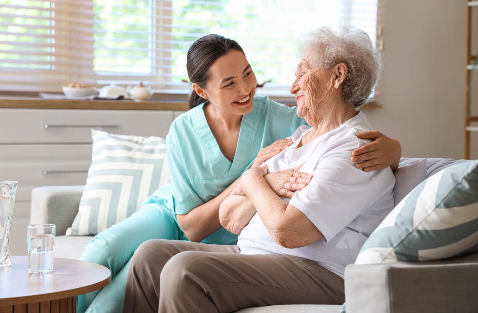 A caregiver hugging an appreciative resident while sitting together on the couch in respite care.