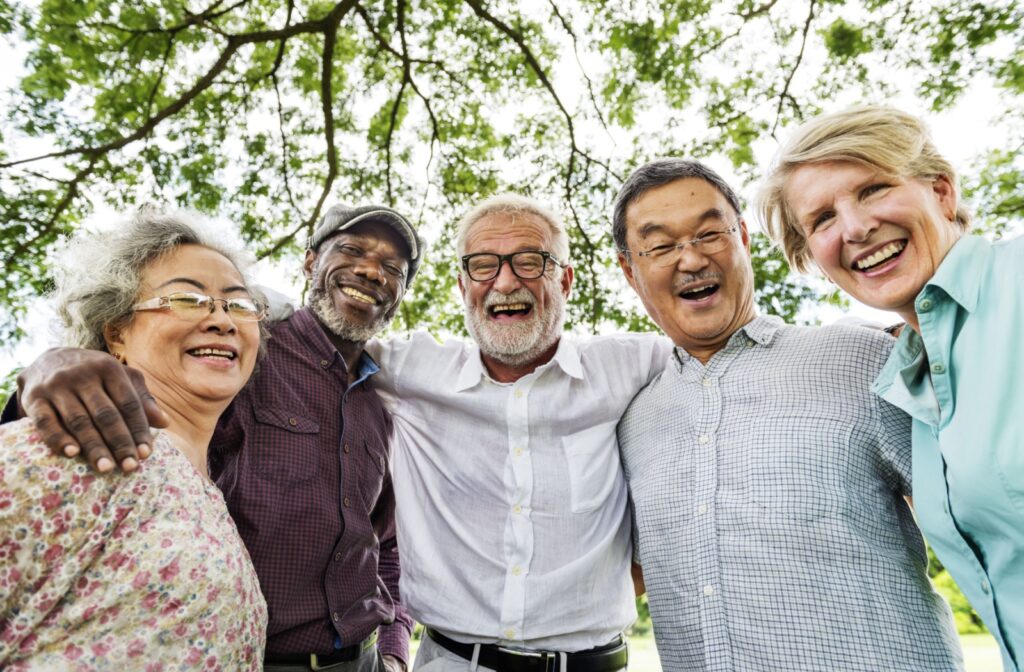 Five seniors stand arm-in-arm, laughing and smiling while enjoying the outdoor areas of their long-term care community